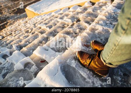 Pericolo di slittamento. Stivali femmina su superficie di ghiaccio con scivolone ruvido. Una donna in pelle marrone scarpe discende la scala di ghiaccio scivoloso. Foto Stock