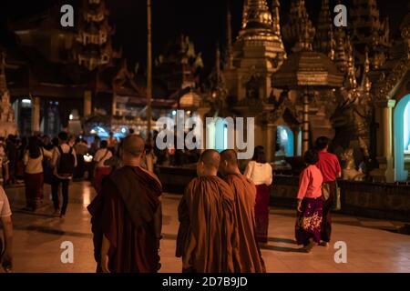 Yangon, Myanmar - 30 dicembre 2019: Tre monaci passeggiate intorno alla pagoda Shwedagon e le sue strutture dorate circostanti di notte Foto Stock