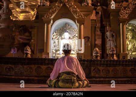 Yangon, Myanmar - 30 dicembre 2019: Una donna prega e medita, seduto di fronte a una statua di buddha alla Pagoda di Shwedagon Foto Stock