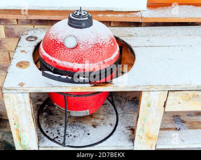 Grigliata rossa in ceramica leggermente spolverata con neve nel foro del tavolo di legno Foto Stock