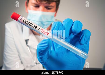 Medico che tiene il campione di test con tampone coronavirus in un flaconcino con guanti e maschera facciale in laboratorio. Primo piano Foto Stock