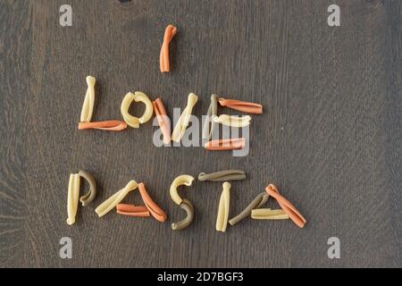 Amo la pasta scritta con la pasta tricolore caserecce italiana su un tavolo di legno, vista dall'alto Foto Stock