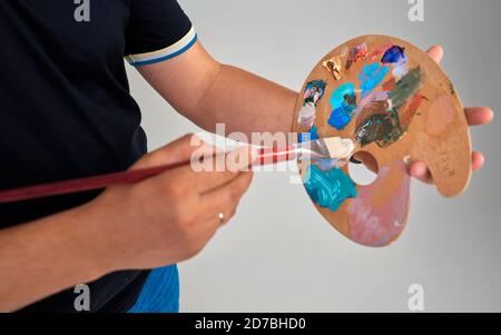 le vernici e i pennelli multicolori giacciono fianco a fianco su uno sfondo bianco. il bambino tiene un pennello in mano Foto Stock