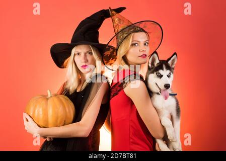 Due giovani donne felici in abiti neri e rossi, costumi streghe halloween sulla festa su sfondo arancione. Due belle donne bionde nel carnevale Foto Stock