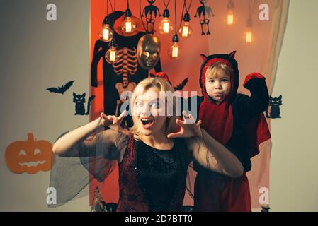 Madre che indossa come strega, figlio che indossa come diavolo. Ragazzo in costume diavolo. Bella giovane donna con un bambino con zucche autunno. Madre e figlio sorridenti Foto Stock