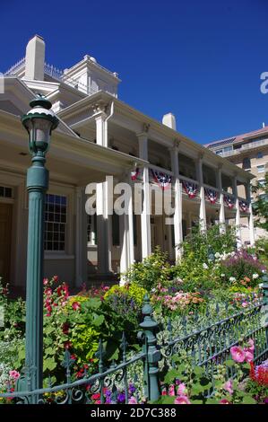 Salt Lake City, UT--12 luglio 2012; casa pioniera in legno centro con giardino di fiori dietro recinzione di ferro verde e ex casa di Brigham Young leader di Foto Stock