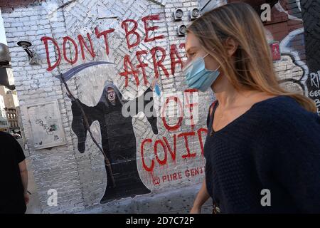 New York City, Stati Uniti. 21 Ott 2020. Una donna che indossa una maschera passa accanto a un murale su Houston Street raffigurante il presidente degli Stati Uniti Donald Trump come il triste reaper come COVID-19 casi continuano a salire negli Stati Uniti, New York, NY, 21 ottobre 2020. Il murale è stato dipinto da un artista che prende il nome di "Genius reale", le parole "non avere paura di Covid" sono state pronunciate dal presidente Trump durante la ripresa dal COVID-19. (Anthony Behar/Sipa USA) Credit: Sipa USA/Alamy Live News Foto Stock