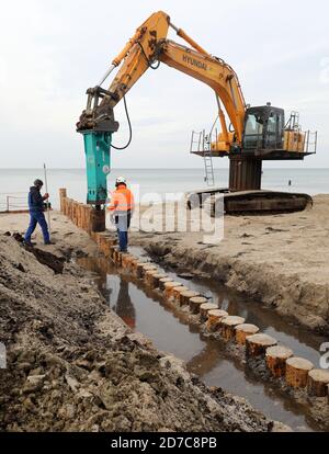 20 ottobre 2020, Meclemburgo-Pomerania occidentale, Graal-Müritz: Un escavatore arieti si accumuli nella spiaggia del Mar Baltico nella brughiera di Rostock, costruendo così il collegamento terrestre per la costruzione di groynes. In totale, 34 vecchi groynes saranno sostituiti da 33 nuovi groynes sulla spiaggia. Nuovi pali di legno duro saranno guidati nell'acqua. Il lavoro sarà completato entro il 31.03.2021 e servirà non solo a proteggere la costa, ma soprattutto a fornire spiagge più ampie ai turisti. Groynes sono dighe che corrono ad angolo retto alla spiaggia. Foto: Bernd Wüstneck/dpa-Zentralbild/ZB Foto Stock