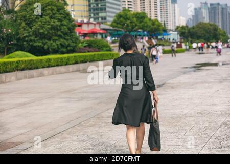 Donna d'affari che cammina via sulla strada della città di Shanghai indossando elegante shirtdress di seta per il professionista del lavoro. La donna d'affari matura si sposti Foto Stock