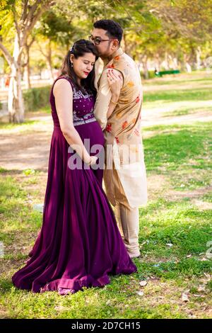 Giovane donna incinta asiatica con suo marito che indossa un abito tradizionale in piedi nel parco o giardino spazio di copia per scrivere testo. Foto Stock