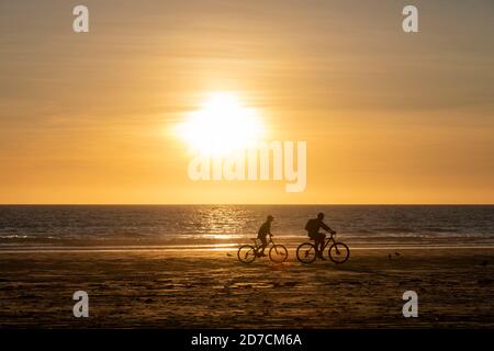 Un padre e un figlio cavalcano le biciclette lungo Cable Beach al tramonto. Foto Stock