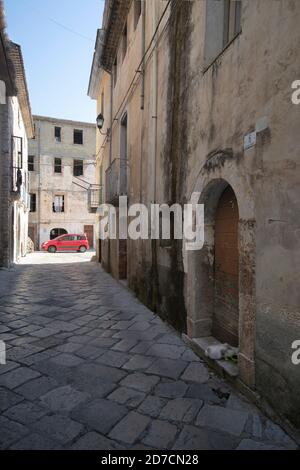 Strada stretta in vecchio towm di Fondi con un rosso parcheggiata l'auto sullo sfondo e un gatto che mangia dentro il primo piano Foto Stock