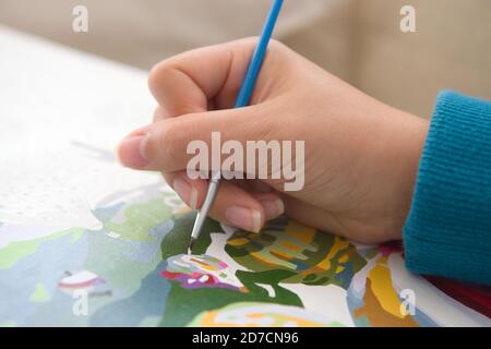 4 - giovane e giovane mano femminile con unghie naturali è mostrata in grande dettaglio tenendo un pennello blu e pittura per numeri. Un hobby popolare. Foto Stock