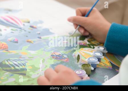 10 - artista al lavoro pittura per numeri. Pentole numerate di vernice mostrate utilizzando la messa a fuoco selettiva. Prospettiva media sulla tela. Tema della mongolfiera Foto Stock