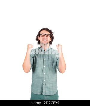 Giovane uomo contentato, capelli lunghi ricci indossa occhiali, mantiene i pugni stretti in alto, guardando verso l'alto con emozione positiva, isolato su sfondo bianco Foto Stock