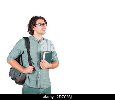 Ritratto di sorridente studente ragazzo tenendo un libro al petto e portando il suo zaino sulle spalle guardando gioioso da parte. Giovane attraente, lungo ricciolo Foto Stock