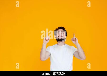 Ritratto di un giovane allegro con una barba che punta le dita verso lo spazio della copia, isolato su uno sfondo giallo Foto Stock