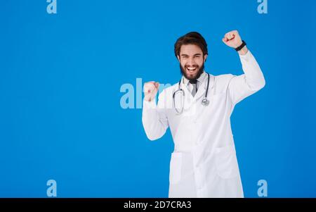 Ritratto di felice eccitato medico in camice medico bianco mostrando sì segno gesto. DOC MAN è riuscito al lavoro. Ragazzo isolato su blu Foto Stock