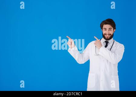 Banner orizzontale di sorridente giovane medico maschile che mostra e presenta qualcosa con la mano, isolato su sfondo blu con spazio di copia a sinistra Foto Stock