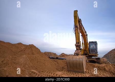 Escavatore durante la costruzione della conduttura principale di approvvigionamento idrico. Posa fognature sotterranee in cantiere. Acqua principale sistema di drenaggio sanitario Foto Stock