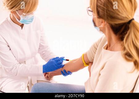 Shot di infermiera femminile che preleva il campione di sangue dal paziente mentre si siede al pankcground bianco isolato. Foto Stock