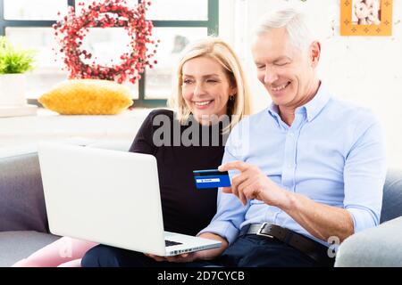 Foto di coppie anziane che acquistano e pagano in modo sicuro online mentre si siede sul divano a casa. Foto Stock
