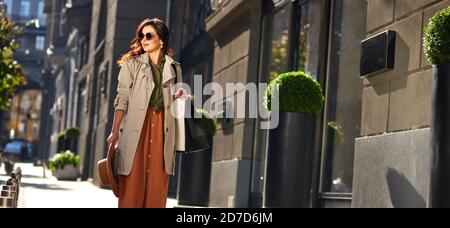 Giovane donna alla moda con borsa per lo shopping che cammina per le strade della città in una calda giornata autunnale, visitando boutique di moda e negozi, banner panoramico. Moda, concetto di stile di vita della gente Foto Stock