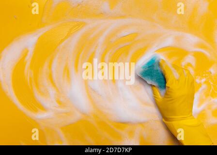 pulire la schiuma su uno sfondo giallo con una spugna blu. Foto Stock