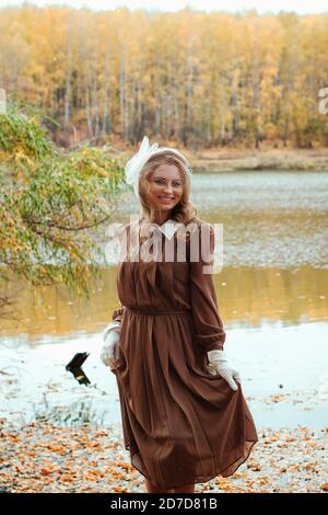 Ritratto di giovane donna in abito retrò sorridente vicino al lago in autunno Foto Stock