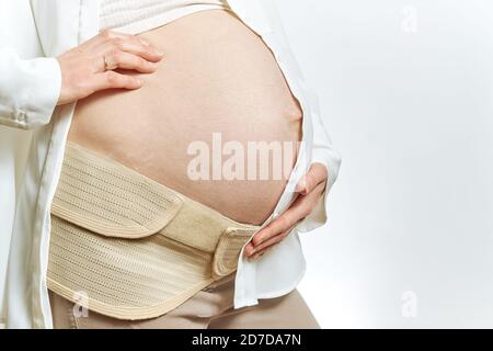 Donna incinta pancia senza volto e mani da vicino isolato. Cintura di maternità gravidanza supporto addome Binde. Addominale vista laterale e spazio di copia. Foto Stock