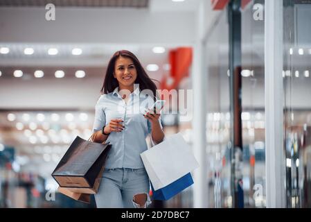 Donna brunette nel supermercato con molti pacchetti e. telefono in mani hanno shopping giorno Foto Stock