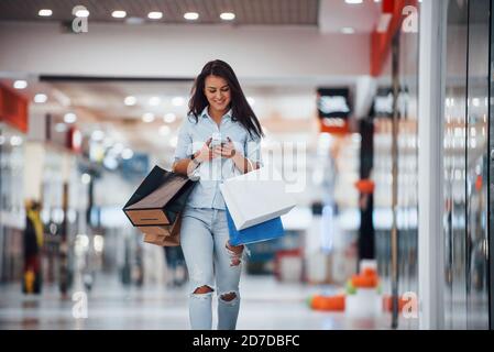 Donna brunette nel supermercato con molti pacchetti e. telefono in mani hanno shopping giorno Foto Stock