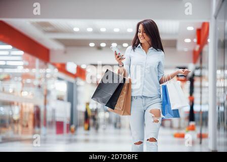 Donna brunette nel supermercato con molti pacchetti e. telefono in mani hanno shopping giorno Foto Stock