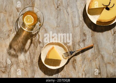 Vista dall'alto di un pezzo di torta al limone con tè sotto luce solare diretta con ombre dure sul tavolo Foto Stock