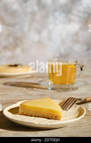 Pezzo di crostata di limone con tè sotto la luce diretta del sole con ombre dure sul tavolo Foto Stock