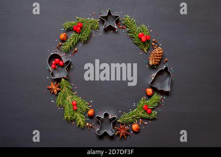 Corona di Natale realizzata con stampi per biscotti, spezie e un albero di Natale su sfondo nero con spazio per la copia. Foto Stock