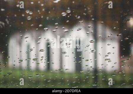 Vista offuscata della fila di case bianche attraverso il parabrezza dell'auto in mattinata di autunno piovosa. Foto Stock