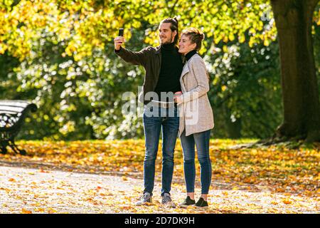 KENSINGTON LONDON, REGNO UNITO 22 OTTOBRE 2020. Una coppia prende un selfie davanti ad una esposizione dei colori autunnali in una mattina soleggiata in Kensington Gardens in contrasto con il giorno prima con la pioggia torrenziale dopo che Storm Barbara ha colpito la capitale.Londra è andato nell'allarme di secondo livello per l'epidemia di Coronavirus (Covid 19) a Londra. Credit: amer Ghazzal/Alamy Live News Foto Stock