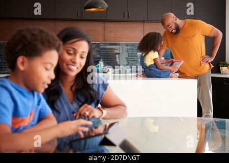 Genitori afroamericani che aiutano i bambini che studiano il lavoro di lavoro sui tablet digitali In cucina Foto Stock