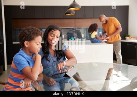 Genitori afroamericani che aiutano i bambini che studiano il lavoro di lavoro sui tablet digitali In cucina Foto Stock