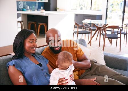 Sorridendo genitori afroamericani coccolarsi e giocare con Baby Daughter Interni sul divano a casa Foto Stock