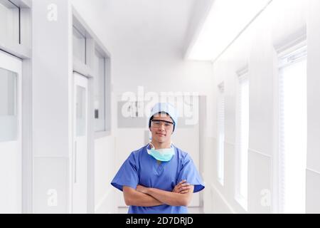 Ritratto di giovane medico maschile indossando scrub in piedi in ospedale Corridoio Foto Stock