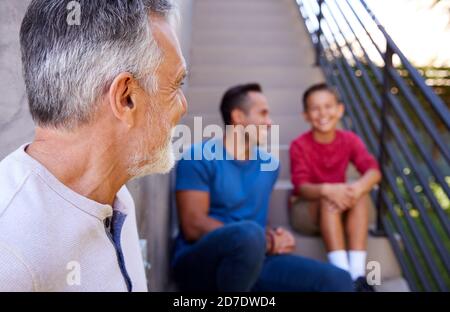 Sorridente Famiglia ispanica maschile Multi-Generation seduta sui gradini in Giardino E parlare insieme Foto Stock