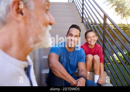 Sorridente Famiglia ispanica maschile Multi-Generation seduta sui gradini in Giardino E parlare insieme Foto Stock