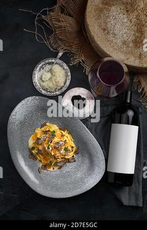 Cucina Italiana - spaghetti al tartufo nero su un piatto grigio e bottiglia di vino. Messa a fuoco selettiva. Verticale. Foto Stock
