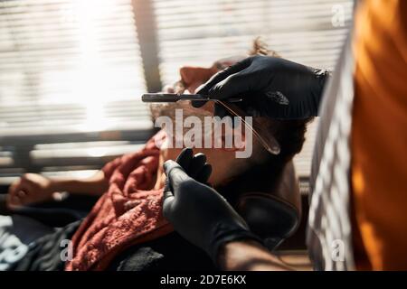 Barbiere in guanti sterili barba per uomo con rasoio dritto Foto Stock