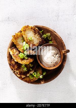 frittelle di patate con yogurt e cipolle verdi e pepe nero. in pentole di argilla su fondo bianco Foto Stock