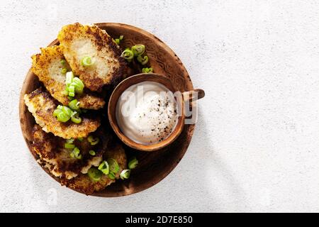 frittelle di patate con yogurt e cipolle verdi e pepe nero. in pentole di argilla su fondo bianco Foto Stock