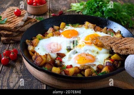 Uova fritte con verdure - shakshuka in una padella e pane di segale su un vecchio sfondo di legno. Colazione tardiva. Stile rustico. Medio-orientale tradizionale Foto Stock