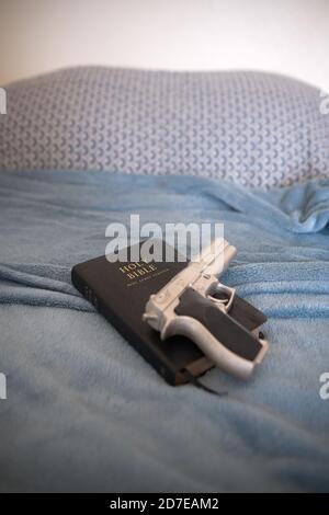 una replica argento berretta 9 mm pistola su una pelle nera La Sacra Bibbia poggia su un letto fatto in una camera da letto a casa di alcuni Foto Stock